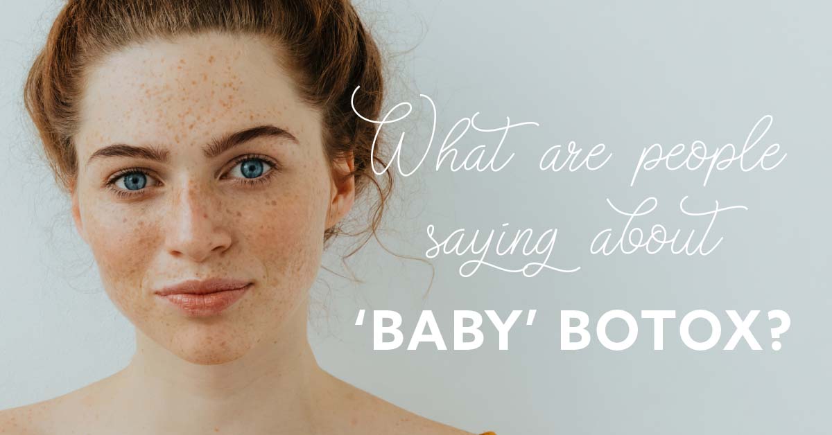 The Skin Center_Baby Botox A red-headed young woman with blue eyes, freckles, and pink lips, stands in front of a baby blue background. Text reads in white cursive:"What are people saying about," followed by white block letters: "'BABY' BOTOX?"